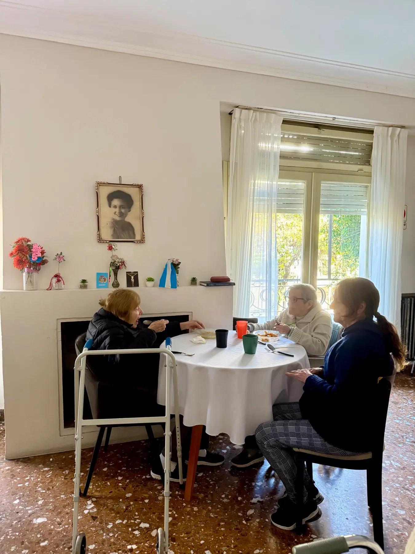 Tres residentes compartiendo la mesa del comedor, bajo el retrato de Margarita