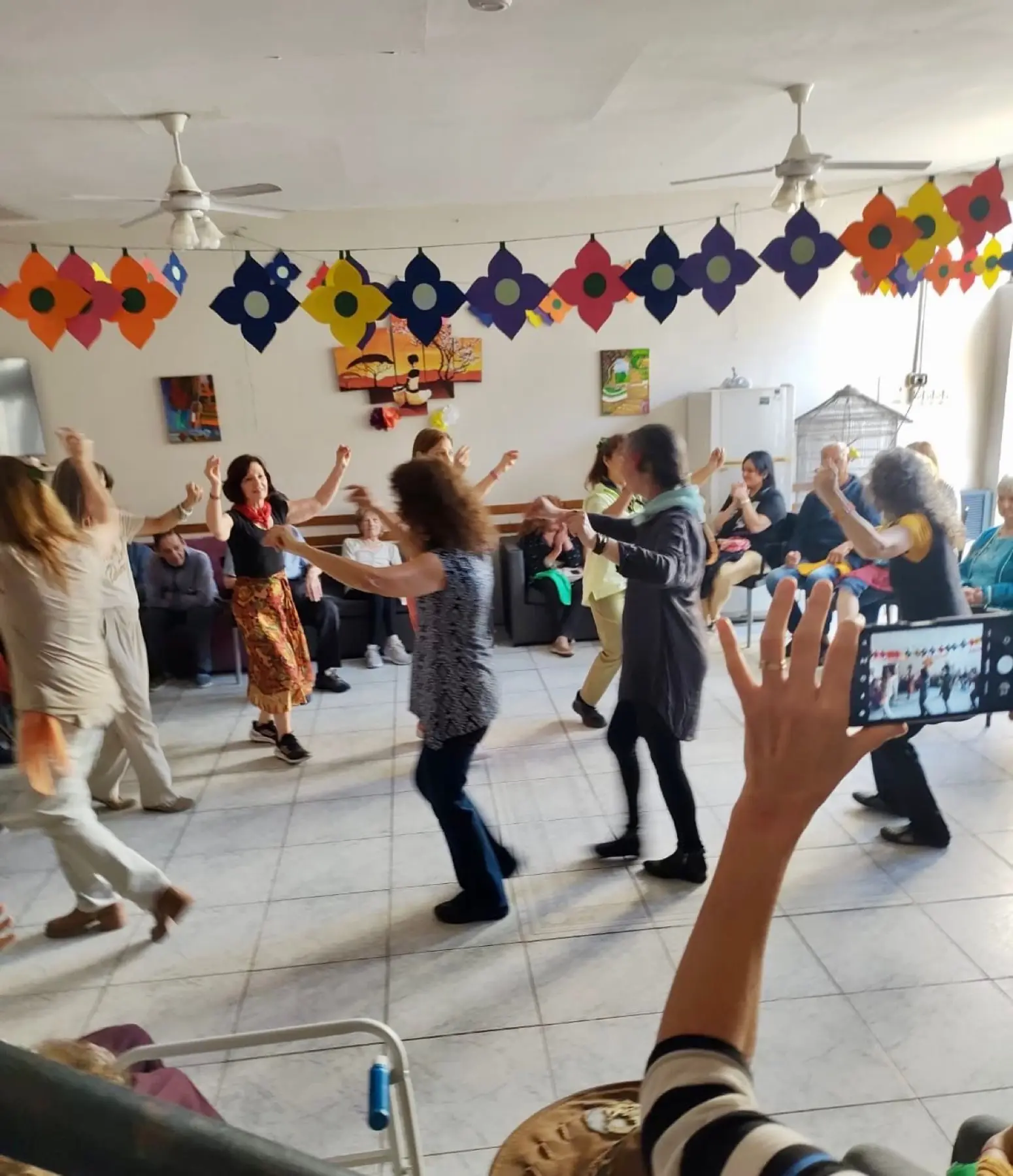Sala de actividades durante un taller de expresión corporal, con guirnaldas de colores y residentes bailando